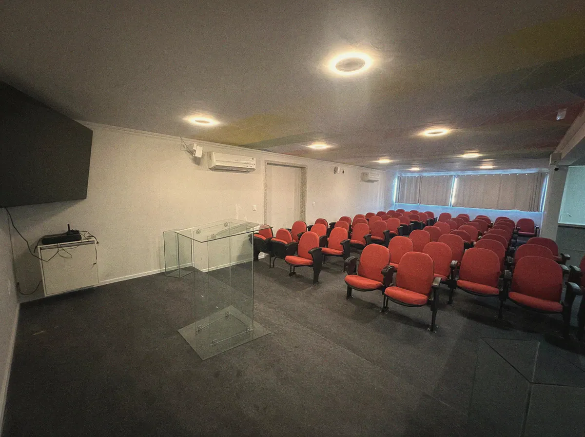 Auditório com fileiras de poltronas vermelhas estofadas e púlpito de vidro